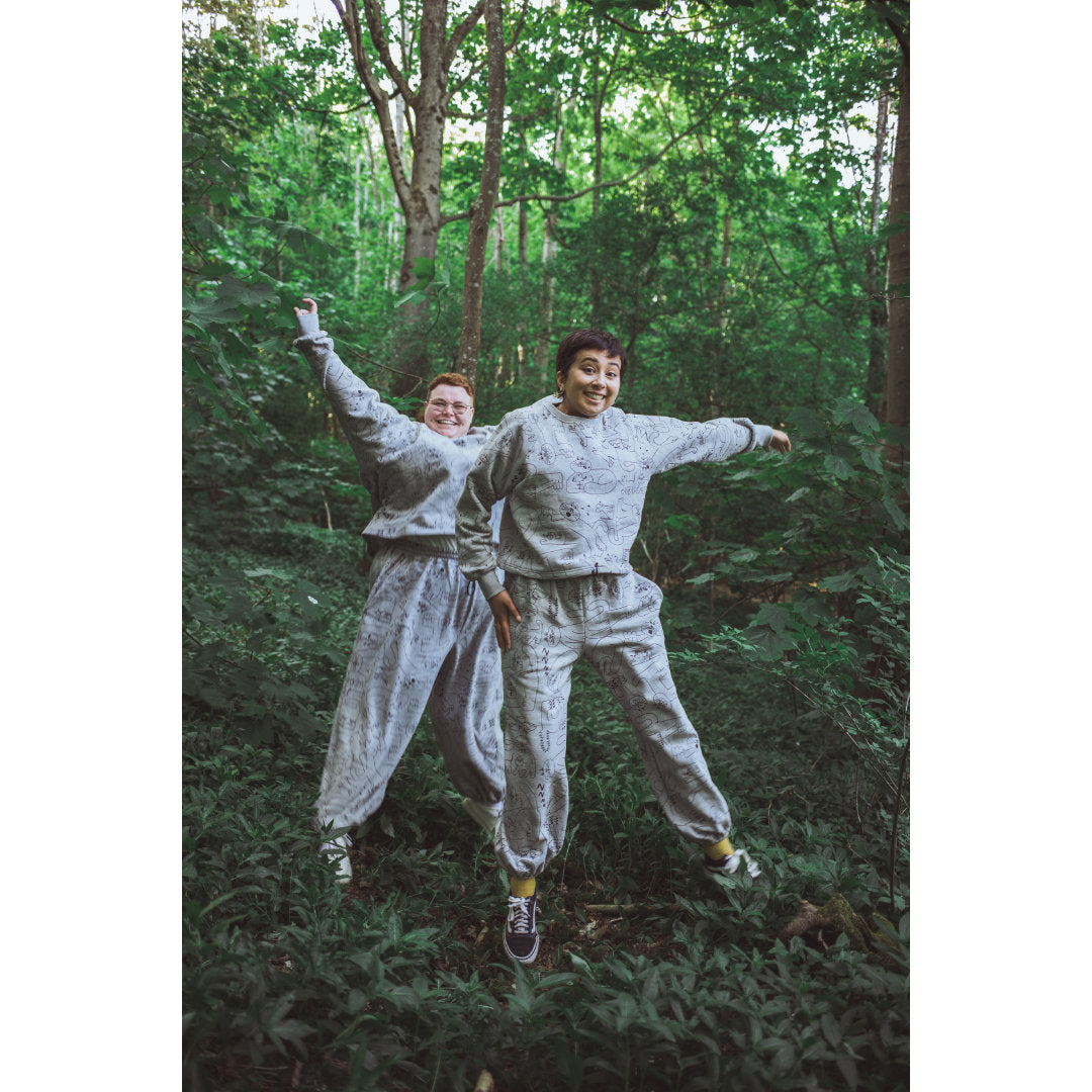 Two people jumping for joy in grey dora the cat print tracksuits by YUK FUN
